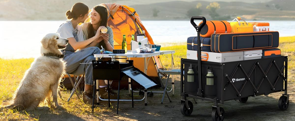 Two women at a campsite by a lake while a collapsible camping wagon filled with gear